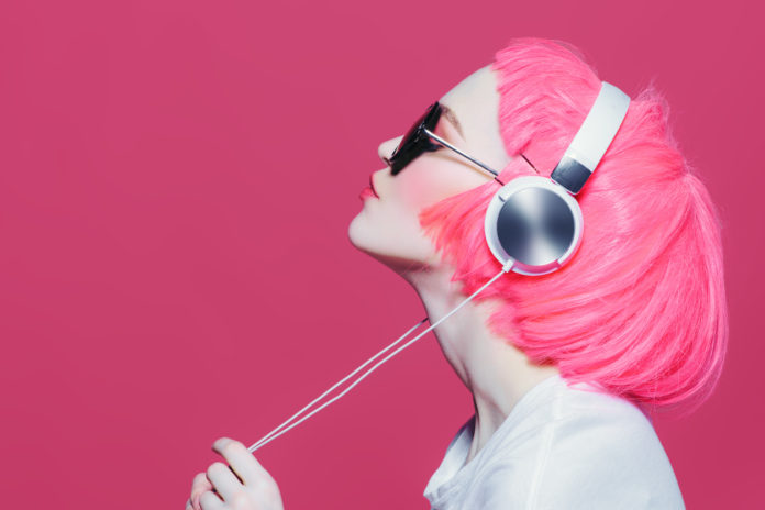 dziewczyna w różowej peruce na różowym tle słuchająca muzyki na słuchawkach nausznych