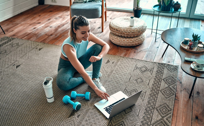 wysportowana dziewczyna z ciężarkami siedząca przed laptopem na dywanie w domu