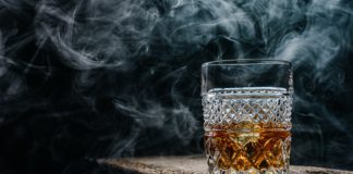 Whisky – jak wybrać ten alkohol? szklanka whisky na drewnianym stole w zadymionym pomieszczeniu